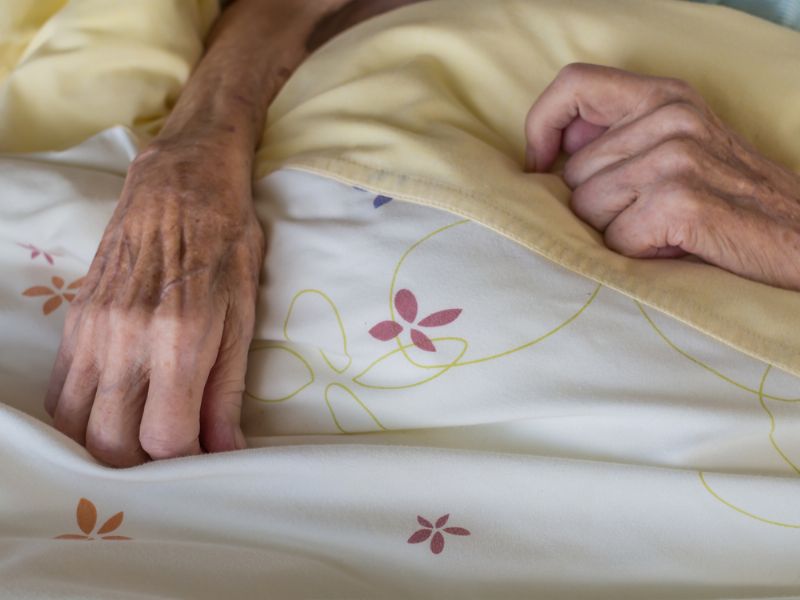 Old woman's hands resting on top of duvet